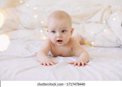 Cute funny baby lying under the blanket on bed. Baby  girl learning to crawl and playing in white sunny bedroom.  Little child doing tummy time. 