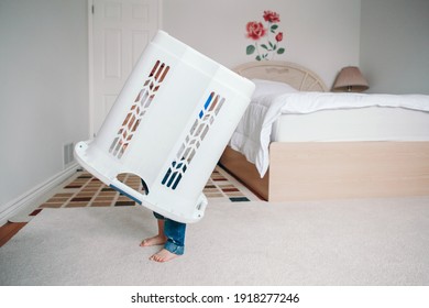 Cute funny baby toddler child with large clothes bin on head. Lonely autistic kid playing alone at home hide and seek game. Funny memorable childhood moment. Home authentic lifestyle. 