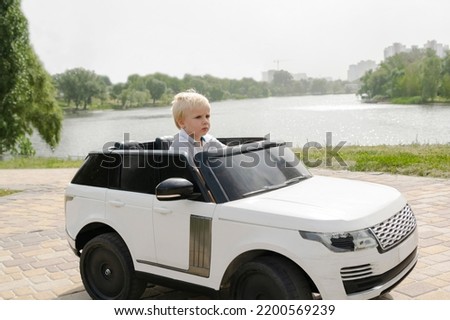 Cute funny blond little young toddler kid child boy sitting,driving,riding in electric toy car,automobile,jeep in park.Children physical,emotional development,childhood daycare,kindergarten concept