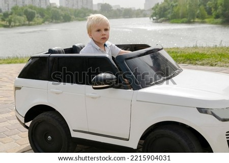Cute funny blond little young toddler kid child boy sitting,driving,riding in electric toy car,automobile,jeep in park.Children physical,emotional development,childhood daycare,kindergarten concept