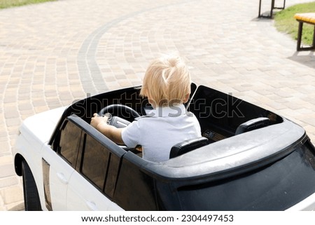 Cute funny blond little young toddler kid child boy sitting,driving,riding in electric toy car,automobile in park.Children physical,emotional development,childhood daycare,kindergarten concept