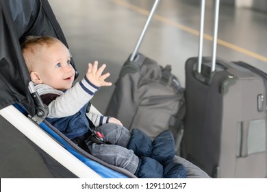 Cute funny caucasian baby boy sitting in stroller near luggage at airport terminal. Child sin carriage with suitcasese near check-in desk counter. Travelling with small children concept