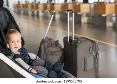 Cute Funny Caucasian Baby Boy Sitting In Stroller Near Luggage At Airport Terminal. Child Sin Carriage With Suitcasese Near Check-in Desk Counter. Travelling With Small Children Concept