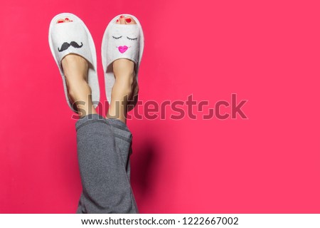 Cute funny couple on pink red. Woman wearing bright pants lying with legs upwards wearing unusual slippers with faces of man and woman