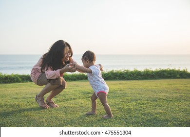 Cute funny happy baby making his first steps on a green grass, mother holding her hands supporting by learning to walk - Powered by Shutterstock