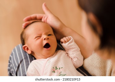 Cute funny infant baby girl making faces lying on mother hands in room at home and try to fall asleep. Motherhood. Woman holding newborn 