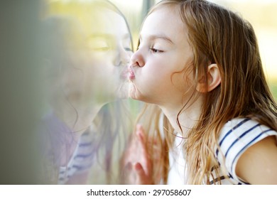 Cute Funny Little Girl Kissing Her Reflection On A Window Glass