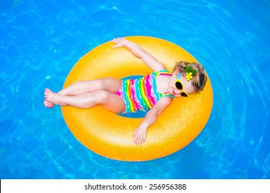 Cute Funny Little Toddler Girl In A Colorful Swimming Suit And Sun Glasses Relaxing On An Inflatable Toy Ring Floating In A Pool Having Fun During Summer Vacation In A Tropical Resort 