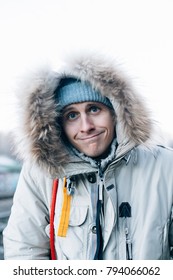 Cute And Funny Looking Young Man In Huge Furry Hood From Winter Jacket Makes Silly Face Expression, Saying Oh Well What Can I Do Or I Am Sorry. Looks Straight Into Camera And Smiles