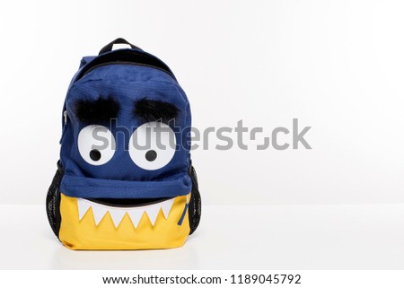 Cute funny monster backpack on white desk, open school bag