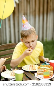 Cute Funny Nine Year Old Boy Celebrating His Birthday With Family Or Friends And Eating Homemade Baked Cake In A Backyard. Birthday Party For Kids