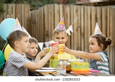 Cute Funny Nine Year Old Boy Celebrating His Birthday With Family Or Friends With Homemade Baked Cake In A Backyard. Birthday Party. Kids Wearing Party Hats, Clink Paper Caps