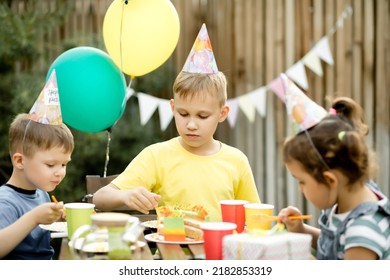 Cute Funny Nine Year Old Boy Celebrating His Birthday With Family Or Friends And Eating Homemade Baked Cake In A Backyard. Birthday Party For Kids