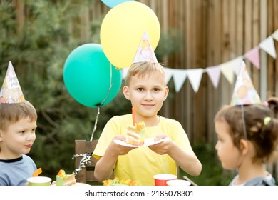 Cute Funny Nine Year Old Boy Celebrating His Birthday With Family Or Friends And Eating Homemade Baked Cake In A Backyard. Birthday Party For Kids