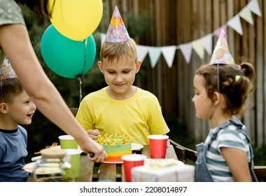 Cute Funny Nine Year Old Boy Celebrating His Birthday With Family Or Friends And Eating Homemade Baked Cake In A Backyard. Birthday Party For Kids