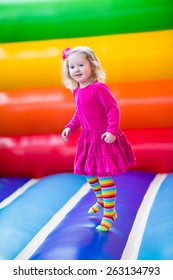 Cute funny preschool little girl in a colorful dress playing, jumping and bouncing in an inflatable castle having fun at a children birthday party on a kids playground in summer