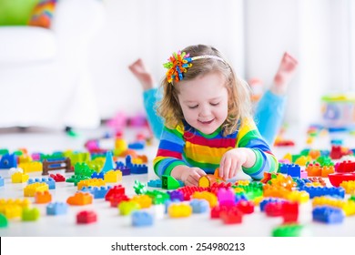Cute funny preschooler little girl in a colorful shirt playing with construction toy blocks building a tower in a sunny kindergarten room. Kids playing. Children at day care. Child and toys.
