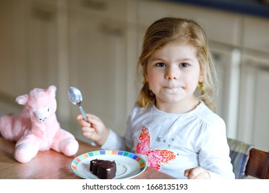 Cute Funny Toddler Girl Eating Chocolate Ice Cream At Home. Happy Healthy Baby Child Feeding Plush Lama Toy With Sweet Ice-cream. Lovely Kid Enjoying Dessert Pudding.