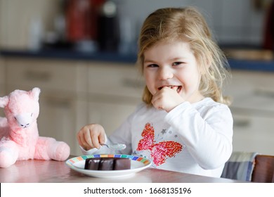 Cute Funny Toddler Girl Eating Chocolate Ice Cream At Home. Happy Healthy Baby Child Feeding Plush Lama Toy With Sweet Ice-cream. Lovely Kid Enjoying Dessert Pudding.