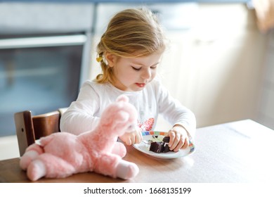 Cute Funny Toddler Girl Eating Chocolate Ice Cream At Home. Happy Healthy Baby Child Feeding Plush Lama Toy With Sweet Ice-cream. Lovely Kid Enjoying Dessert Pudding.