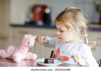 Cute Funny Toddler Girl Eating Chocolate Ice Cream At Home. Happy Healthy Baby Child Feeding Plush Lama Toy With Sweet Ice-cream. Lovely Kid Enjoying Dessert Pudding.