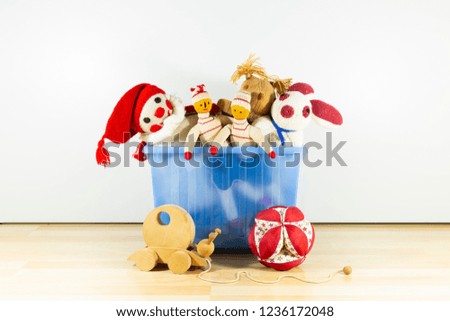 Cute and funny vintage children toys in a blue plastic box in front of a white wall. Assortment consists of a buffoon, a bunny, puppets, a squirrel, a wooden snail and a ball.