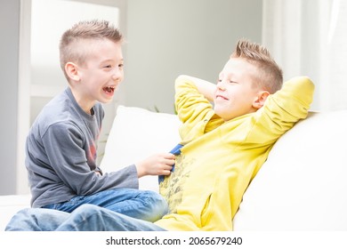 Cute funny young boy laughing at his brother as he tries to tickle him while they relax on the couch together at home