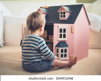 A cute gender confident little boy is busting stereotypes and socially imposed expectations by playing with a big pink doll house and having a great time