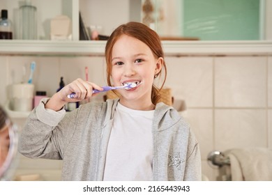 Cute ginger baby girl brushing her teeth and looking to the camera - Powered by Shutterstock