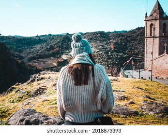 A Cute Girl From Behind Wearing A Cozy Sweater And A Pompom Beanie Hat, Relaxing Near A Church In The Countryside