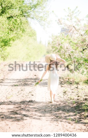 Cute girl with blond hair in a white sundress in spring in a lush garden with daffodils

