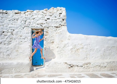 Cute girl in blue dress having fun outdoors near Paraportiani church. Kid at street of typical greek traditional village with white walls and colorful doors on Mykonos Island, in Greece