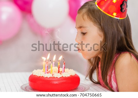 Cute girl celebrating her birthday and blowing candles on cake.