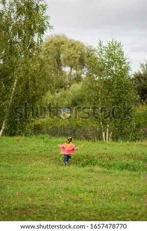 cute girl child 4-5 years old in a pink sweater, a yellow T-shirt and jeans catches giant soap bubbles in nature.