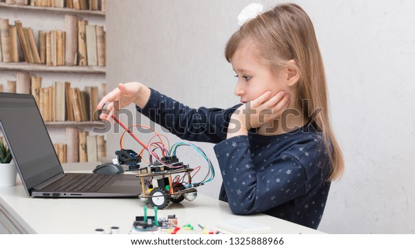 A cute girl collect electronic robot car and\
program it on the computer. The boards and microcontrollers are on\
the table. STEM and STEAM education. Programming. Mathematics.\
Science. Technologie.