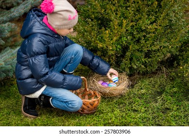 Cute girl collecting colorful Easter eggs in the basket at backyard - Powered by Shutterstock