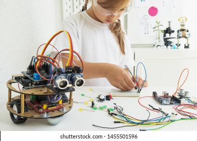 A cute girl constructs metal robot and program it. The boards and microcontrollers are on the table. STEM education inscription. Programming. Mathematics. The science. Technologie. DIY.  - Powered by Shutterstock