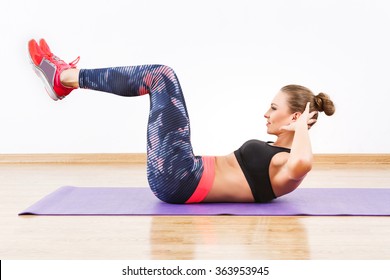 Cute girl with dark hair wearing pink snickers, dark leggings and black short top doing reverse crunch at gym, fitness, white wall and wooden floor. - Shutterstock ID 363953945