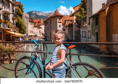 Cute girl discovering the old town of Annecy by bicycle, one of the most popular place to visit in France, pearl of French Alps, French Venice with canals and colorful houses, summer outdoor