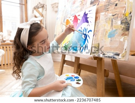 Cute girl drawing with a paint palette and a paintbrush. Little painting artist.