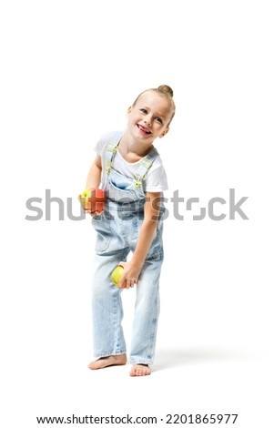 Cute girl dressed in denim overalls fooling around with apples on a white background.
