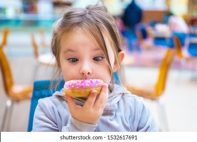 Cute Girl Eating A Donut In A Cafe. Funny Portrait Of A Child