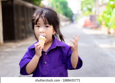 Cute Girl Is Eating An Ice Cream Cone. Children Are Happy To Eat Sweets And Cool. A Young Student Wearing A Purple Sports Uniform. Kid Aged 3-4 Years Old.