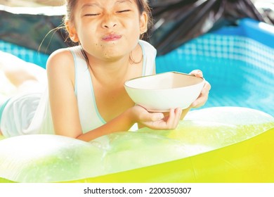 Cute Girl Eating Sweets, Sloppy Mouth On A Rubber Raft Floating On The Pool.On A Blurry Background.