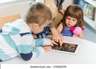 Cute girl with friends using digital tablet at table in school library - Powered by Shutterstock