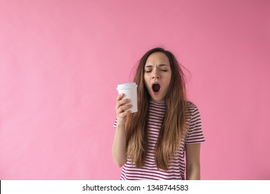 Cute girl with a glass of coffee in hand is yawning. She can't wake up.