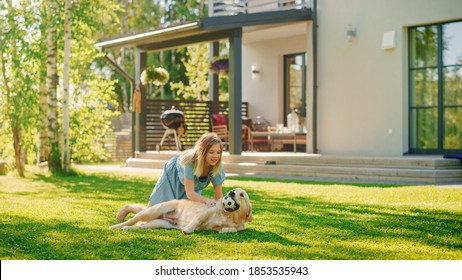 Cute Girl Has Fun With Happy Golden Retriever Dog On The Backyard Lawn. She Pets, Play, Tackle It On The Ground And Scratches Back. Happy Dog Plays With Toy Ball. Idyllic Summer House.