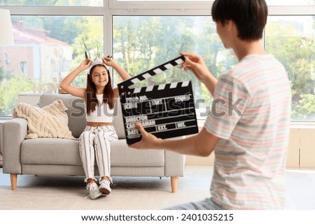 Cute girl and her brother with clapperboard having fun at home
