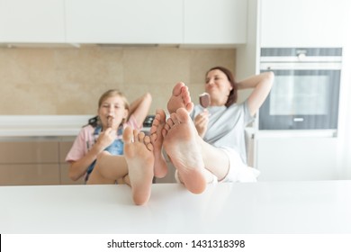 Cute Girl And Her Mother Are Smiling While Eating Ice Cream In The Kitchen With Legs On A Table