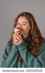 A cute girl is holding a cake-candle. Red-haired happy girl on a gray background - Shutterstock ID 2315229221